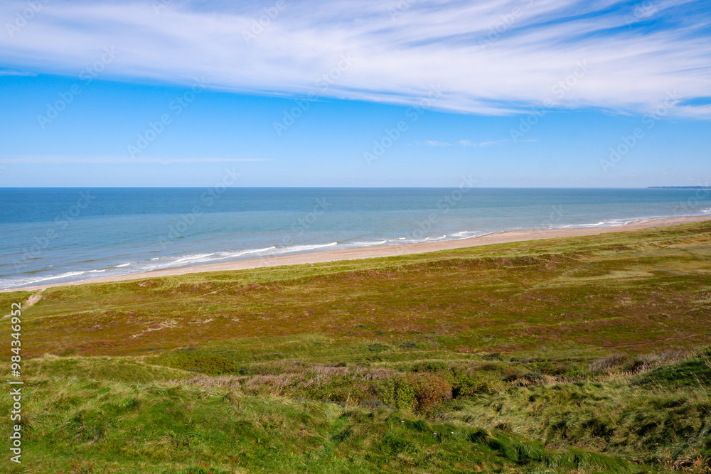 Danish Coastal Landscape. Hilly coast of the northern sea. Sun, blue sky, clouds, waves and grass. Beautiful landscape summer on the northern sea