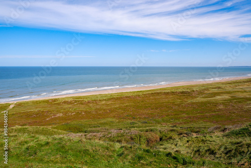 Danish Coastal Landscape. Hilly coast of the northern sea. Sun, blue sky, clouds, waves and grass. Beautiful landscape summer on the northern sea