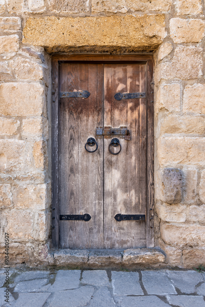 A weathered wooden door with iron hardware stands firmly within a crumbling stone wall, reflecting the charm of a historic area. The rustic features tell a tale of old-world craftsmanship A weathered wooden door with iron hardware stands firmly within a crumbling stone wall, reflecting the charm of a historic area. The rustic features tell a tale of old-world craftsmanship