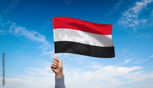 Hand holding Yemen national flag on blue sky. photo