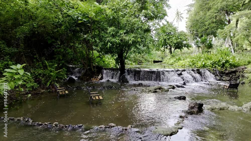 A small waterfall in the Thai countryside with wooden chairs from a coffee shop for sitting and taking pictures in the water flowing by.
A small waterfall in the Thai countryside with wooden chairs from a coffee shop for sitting and taking pictures in the water flowing by.