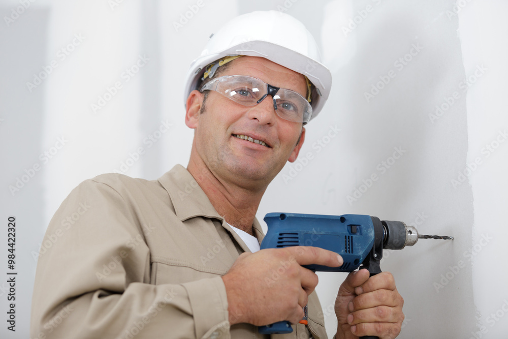 man making hole in wall with drill in white room
