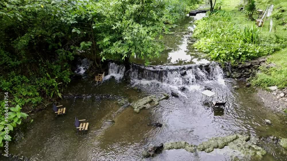 A small waterfall in the Thai countryside with wooden chairs from a coffee shop for sitting and taking pictures in the water flowing by.
A small waterfall in the Thai countryside with wooden chairs from a coffee shop for sitting and taking pictures in the water flowing by.