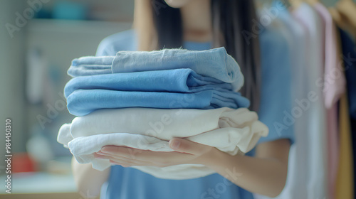  woman is holding a pile of clothes, including a blue shirt and a white shirt. The clothes are stacked on top of each other, and the woman is organizing them. Concept of order and tidiness photo