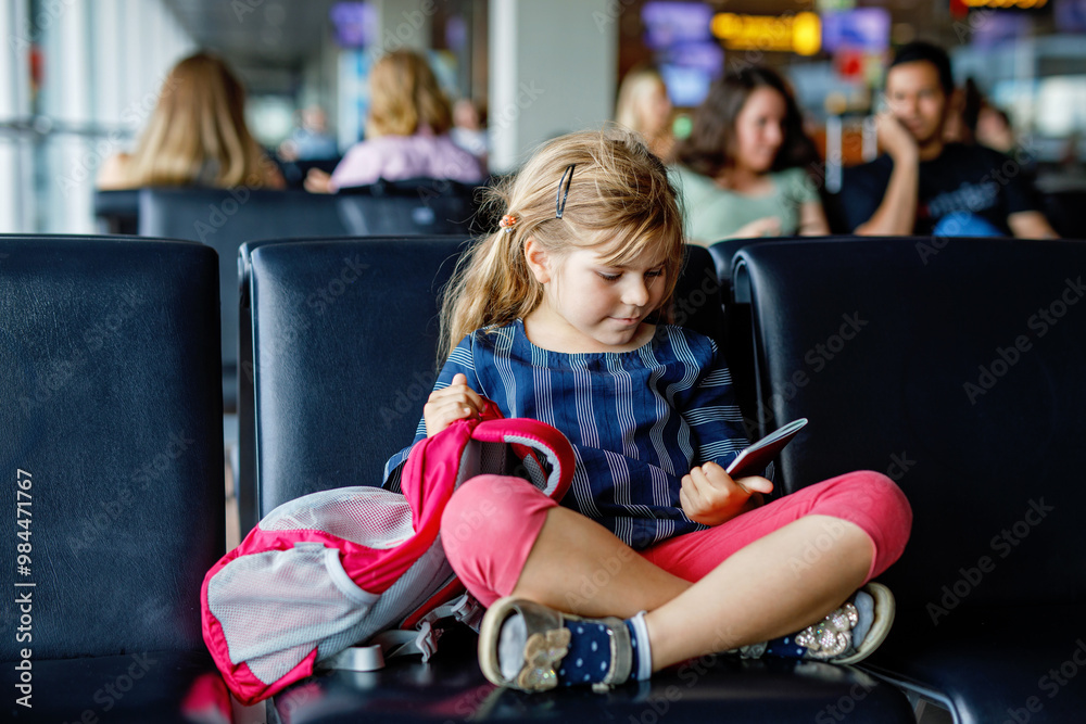 Little girl at the airport waiting for boarding at the big window. Cute kid holding passport..Looking forward to leaving for a family summer vacation Little girl at the airport waiting for boarding at the big window. Cute kid holding passport..Looking forward to leaving for a family summer vacation