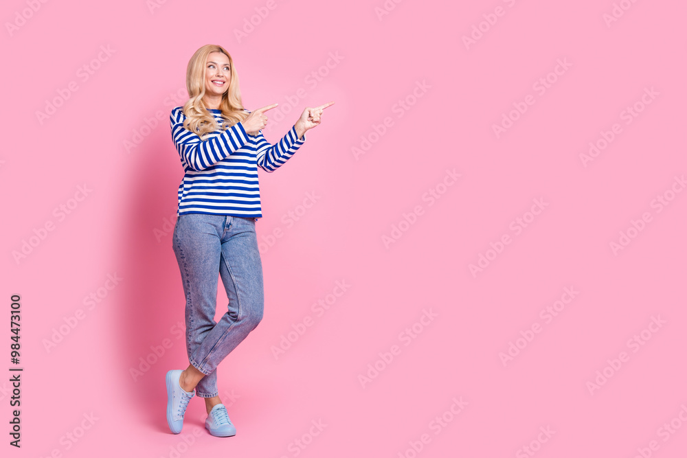 Full body photo of attractive mature woman point look empty space dressed stylish striped clothes isolated on pink color background Full body photo of attractive mature woman point look empty space dressed stylish striped clothes isolated on pink color background