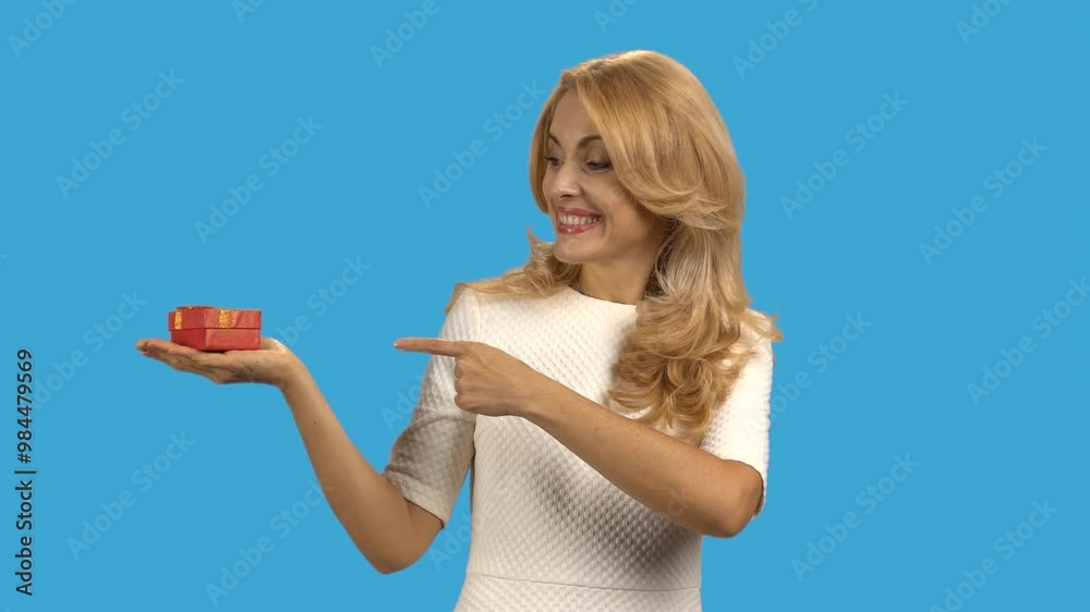 Portrait of a happy mature blonde woman holding a red gift box on her right hand. Birthday or anniversary concept. Isolated on blue. Portrait of a happy mature blonde woman holding a red gift box on her right hand. Birthday or anniversary concept. Isolated on blue.