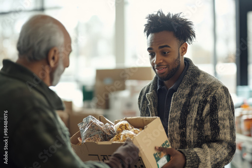 Young adult volunteer is giving a box of food to a senior man in need at a food bank photo