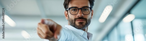 A confident man points decisively while standing in a modern office environment, showcasing leadership and focus.