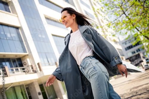 Photo of cheerful pretty lady dressed grey jacket dark eyewear walking enjoying sunshine outdoors town street