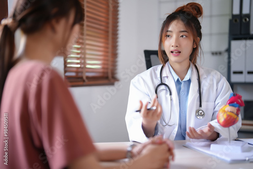 Asian cardiologist doctor women explaining about anatomical of human heart model and giving counseling about medical and mental health therapy to female patient after examining health in hospital