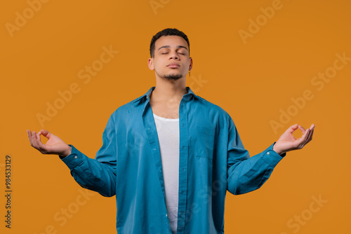 Calm teen guy relaxing, meditating, refuses stress. Breathes deeply on Yellow photo