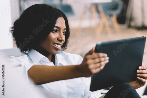 Happy smiling afro american female blogger feeling good from received email with information about notification for new modern touch pad while taking rest at own apartment with cozy interior