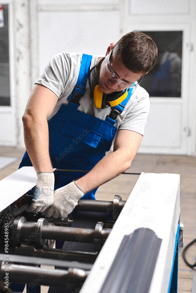 Professional engineer man in blue uniform works in factory. Rolled metal, metal processing and manufacturing of metal fence Professional engineer man in blue uniform works in factory. Rolled metal, metal processing and manufacturing of metal fence