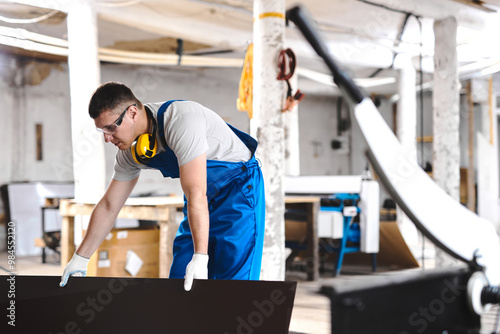 Professional engineer man in blue uniform works in factory. Rolled metal, metal processing and manufacturing of metal fence