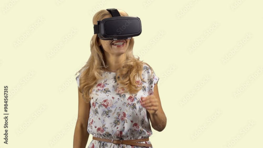 Happy blonde caucasian woman wears virtual reality headset. Isolated on light yellow.