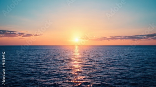 A serene sunset over the deep blue sea, with the sun casting a warm golden glow across the horizon, while the sky blends shades of orange and pink.