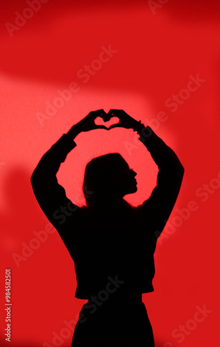 black profile of a girl on a red background with her hands forming a heart above her head photo