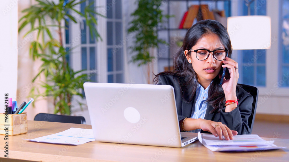 Indian asian young business woman working on laptop and speaking on phone at workplace Indian asian young business woman working on laptop and speaking on phone at workplace
