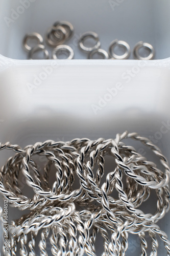Close-up macro shot of small silver jewelry pieces lying in a white mesh box. DIY jewelry