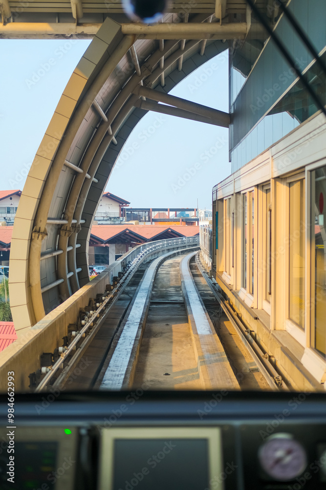 View from inside airport train shows tracks curving ahead through a tunnel, with control panel in foreground, capturing the smooth journey and modern transit experience.