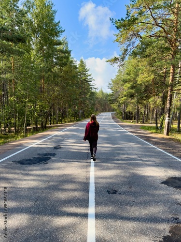 Woman Walking Freely Down an Empty Country Road Surrounded by Pine Trees