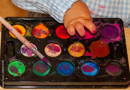 a child's finger picking up finger paint from a watercolor palette photo