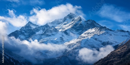 A breathtaking view of snow-covered mountains shrouded in clouds, juxtaposed with a vibrant blue sky, showcasing nature's grandeur.