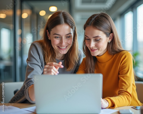 two colleagues at work in a stylish office are discussing in front of a laptop screen