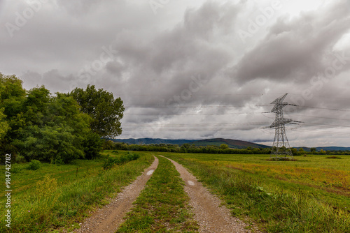 High voltage overhead power line. Green meadow with a cloudy stormy sky