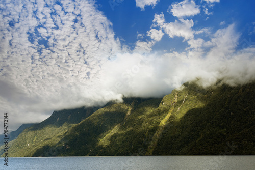 Amazing cloud formation raising over the mountain range at Lake Manapouri early in the morning on a beautiful summer day on a cruise to Doubtful Sound in New Zealand, South Island photo