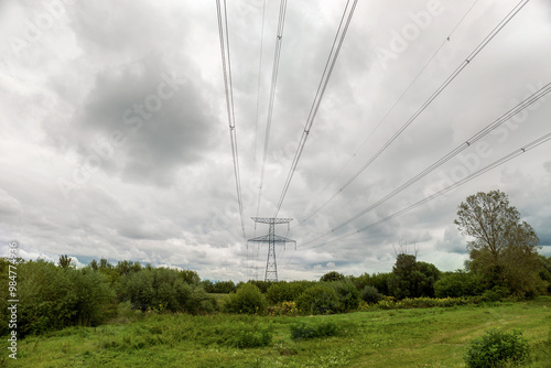 High voltage overhead power line. Green meadow with a cloudy sky