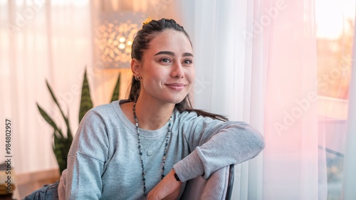 Relaxed Young Woman in Cozy Chair by Window, Enjoying Peaceful Moment. This image evokes feelings of peace, comfort, and home.