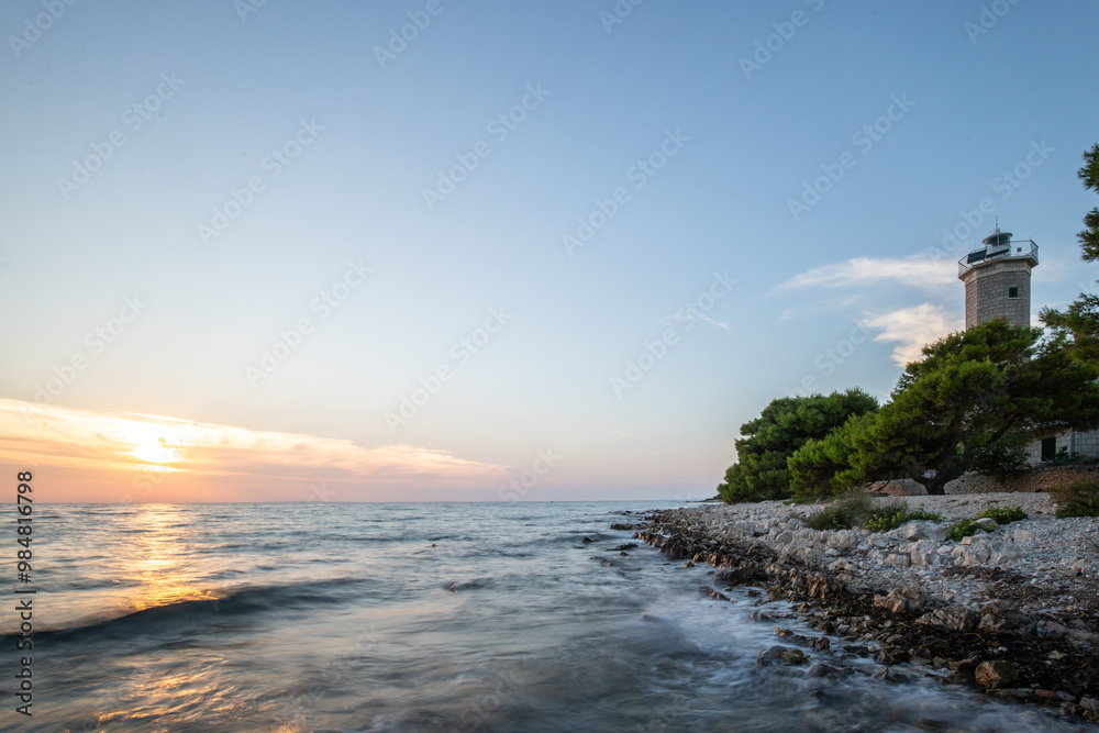 Beautiful sunset in a landscape on a rocky coast with a striking lighthouse and pine forest. View over the coast to the building, on the Mediterranean, Vir, Dalmazien, Croatia, Adriatic Beautiful sunset in a landscape on a rocky coast with a striking lighthouse and pine forest. View over the coast to the building, on the Mediterranean, Vir, Dalmazien, Croatia, Adriatic