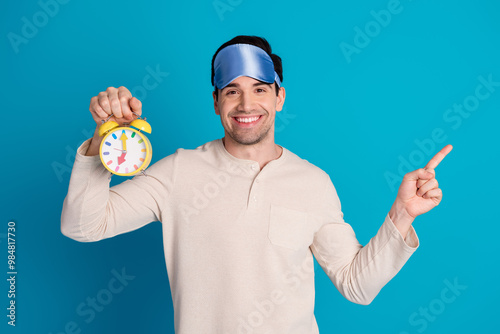 Portrait of nice young man alarm point finger empty space wear pajama isolated on blue color background