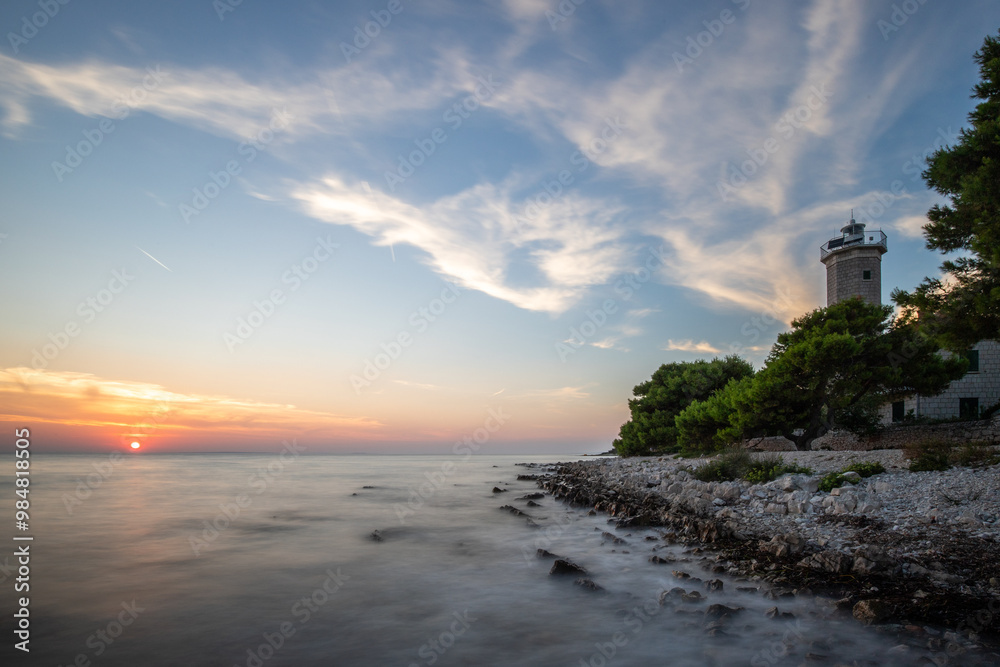 Beautiful sunset in a landscape on a rocky coast with a striking lighthouse and pine forest. View over the coast to the building, on the Mediterranean, Vir, Dalmazien, Croatia, Adriatic Beautiful sunset in a landscape on a rocky coast with a striking lighthouse and pine forest. View over the coast to the building, on the Mediterranean, Vir, Dalmazien, Croatia, Adriatic