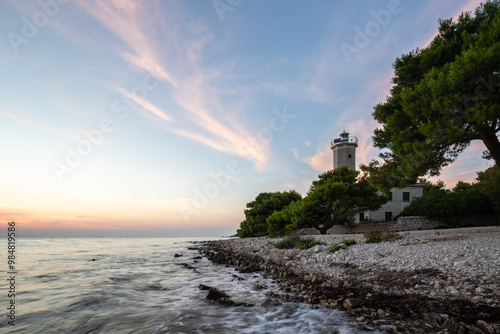 Beautiful sunset in a landscape on a rocky coast with a striking lighthouse and pine forest. View over the coast to the building, on the Mediterranean, Vir, Dalmazien, Croatia, Adriatic