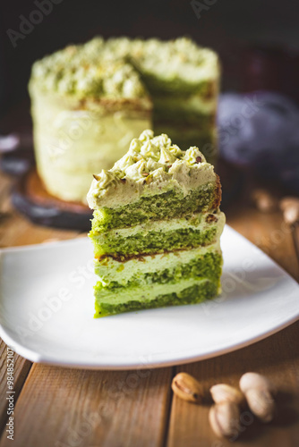 Sweet dessert: pistachio cake. A piece of pistachio cake on a white plate on a wooden table. Vertical photo. Close-up