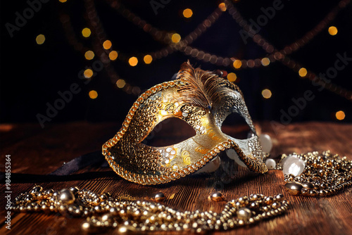 A luxurious gold and silver venetian masquerade mask with intricate detailing, accompanied by sparkling jewelry on a wooden surface. Perfect for a night of mystery and elegance at carnival.  photo