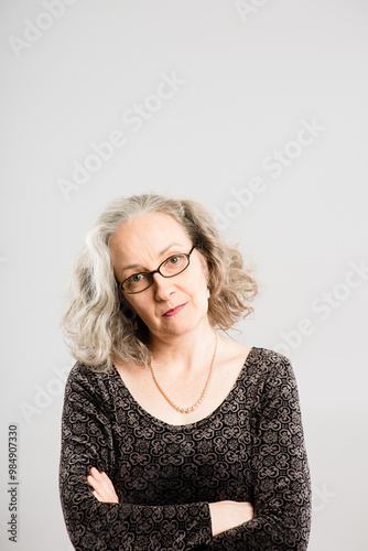 Senior woman, portrait and annoyed face in studio for rude personality, negative mood or upset with glasses. Elderly person, serious and disappointed facial expression on background with crossed arms