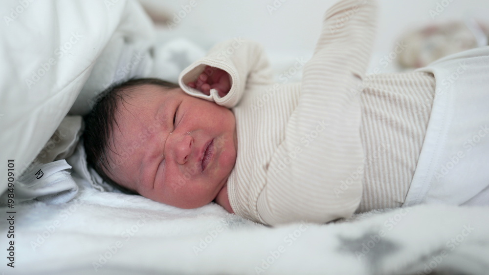 Newborn baby lying in bed, stretching and making a slight grimace, a raw and tender moment of infancy. close-up emphasizes the delicate features and vulnerability of a newborn Newborn baby lying in bed, stretching and making a slight grimace, a raw and tender moment of infancy. close-up emphasizes the delicate features and vulnerability of a newborn
