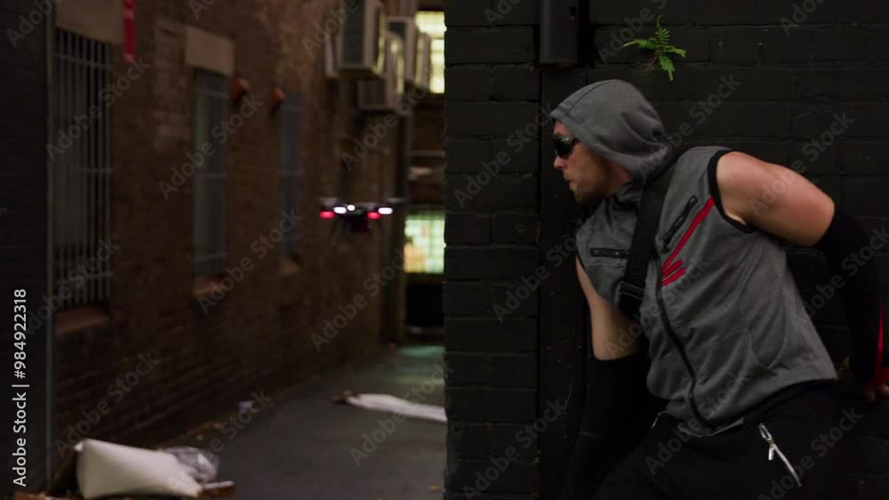Hooded man hiding and grabbing small drone in alleyway - steady cam