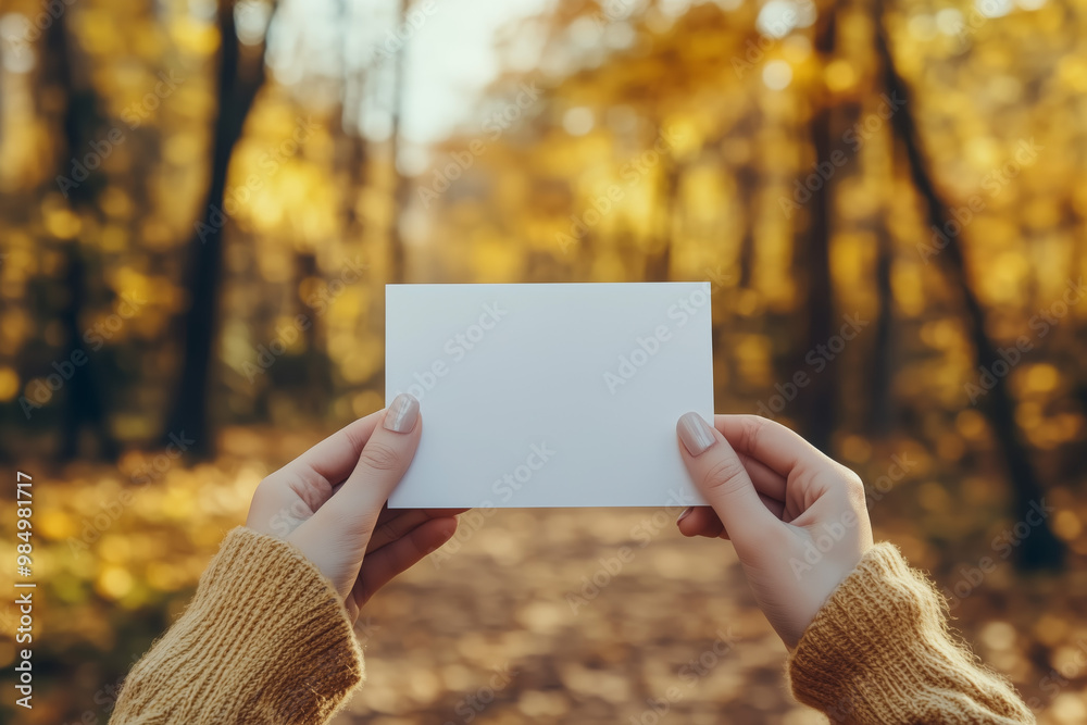 Photo of a woman's hands holding a white small blank sheet of paper, sunny autumn or fall forest on the background Photo of a woman's hands holding a white small blank sheet of paper, sunny autumn or fall forest on the background