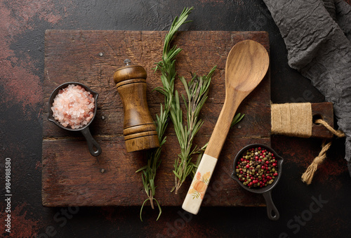 Fototapeta Naklejka Na Ścianę i Meble -  Culinary composition with kitchen utensils and seasonings including Himalayan salt, colorful peppers, fresh rosemary and a wooden spice grinder. Top view