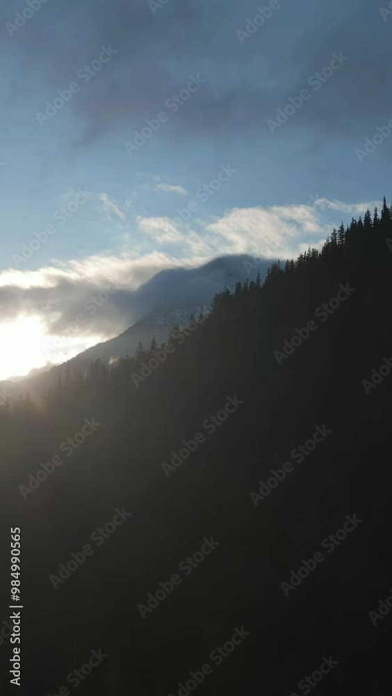 Clouds moving over a snow-capped mountain peak. The sun is setting, casting a warm glow over the scene. British Columbia, Canada. Clouds moving over a snow-capped mountain peak. The sun is setting, casting a warm glow over the scene. British Columbia, Canada.