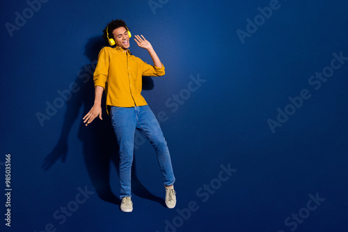 Full body portrait of nice young man dance headphones wear yellow shirt isolated on dark blue color background photo