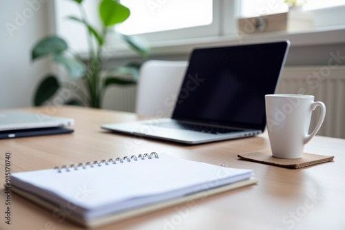 Laptop, notepad, and coffee cup on a wooden desk.