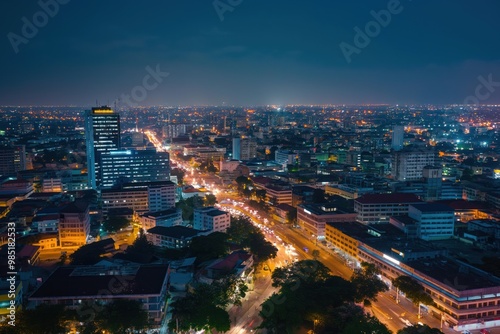 Nighttime aerial view of Accra city, Ghana. Cityscape with modern architecture, old buildings, and infrastructure like roads, bridges, and railways. People are visible on streets, moving through city.