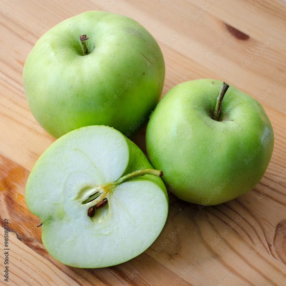 Three Earligold apples on a wood surface, including one cut in half to show the interior Three Earligold apples on a wood surface, including one cut in half to show the interior