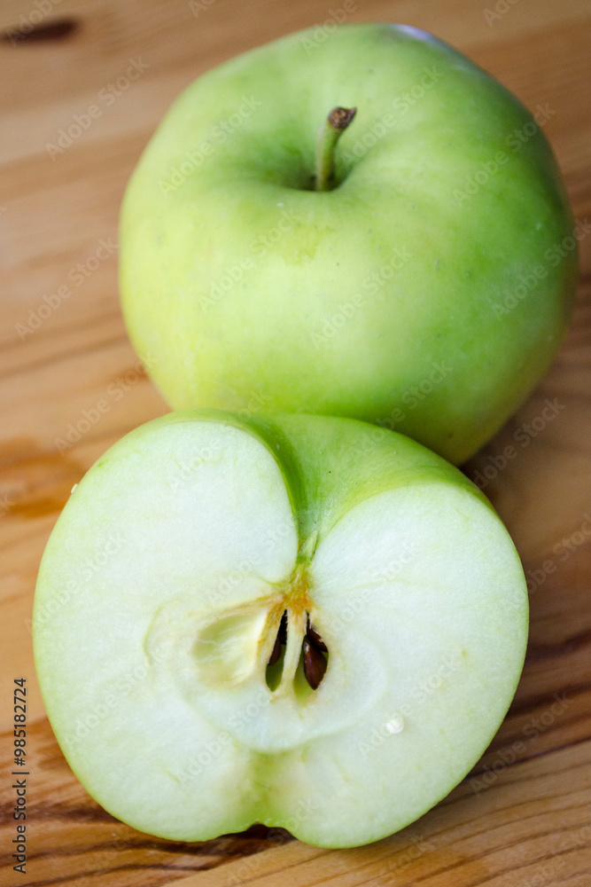 Two Earligold apples on a wood surface, including one cut in half to show the interior Two Earligold apples on a wood surface, including one cut in half to show the interior